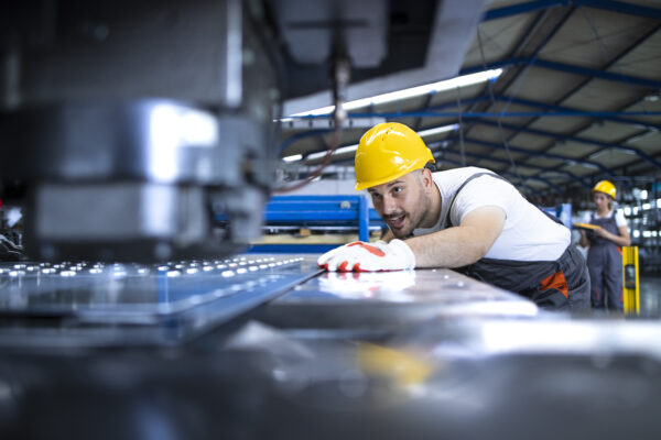 Factory worker in protective uniform and hardhat operating industrial machine at production line.